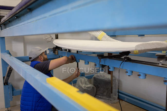 Vue latérale de l'homme caucasien faisant une planche de surf dans l'atelier — Photo de stock