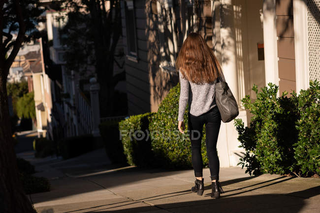 Vista posteriore della donna che cammina per strada in una giornata di sole — Foto stock