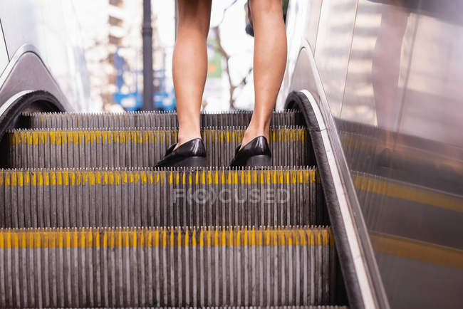 Coupe basse des jambes féminines debout sur l'escalator — Photo de stock