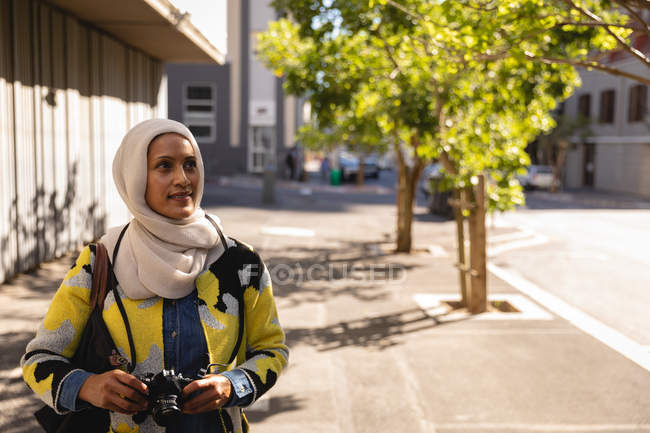 Front view of a thoughtful young mixed-race woman standing on street with digital camera — Stock Photo
