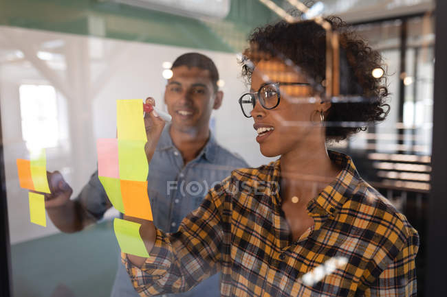 Frontansicht glücklicher Geschäftsleute mit gemischter Rasse, die auf klebrigen Zetteln im modernen Büro stehen — Stockfoto