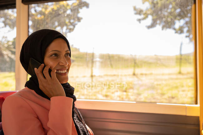 Vista lateral de una hermosa mujer de raza mixta hablando por teléfono móvil mientras viaja en autobús - foto de stock
