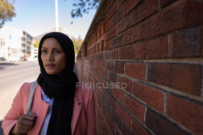Front view of thoughtful Mixed race woman walking on sidewalk next to a brick wall — Stock Photo