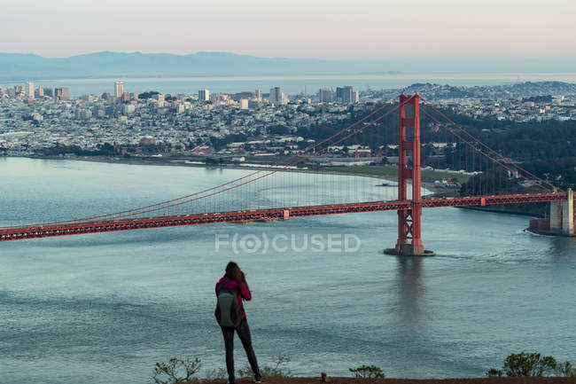 Visão traseira da mulher tirando uma foto de uma ponte em um dia ensolarado — Fotografia de Stock