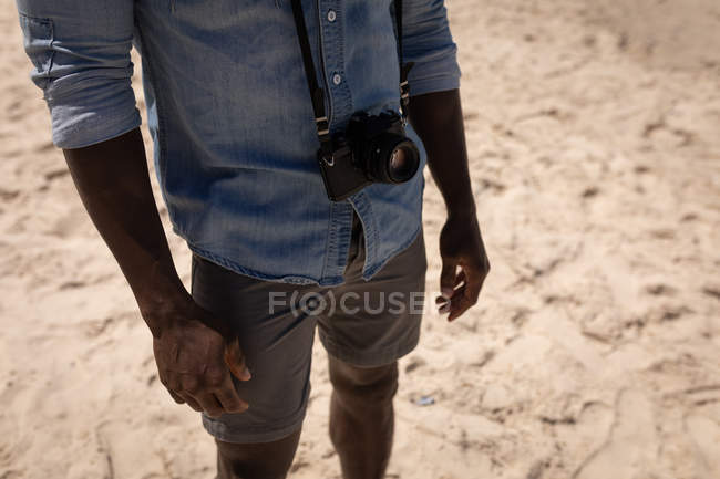 Partie médiane de l'homme debout avec caméra à la plage par une journée ensoleillée — Photo de stock