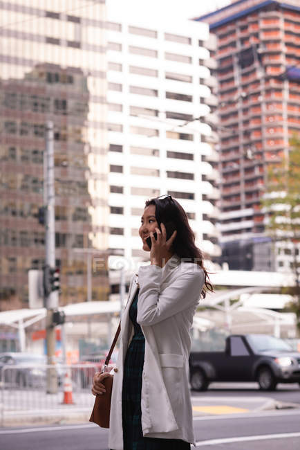Вид сбоку на азиатскую женщину, разговаривающую по мобильному телефону, стоя на улице — стоковое фото