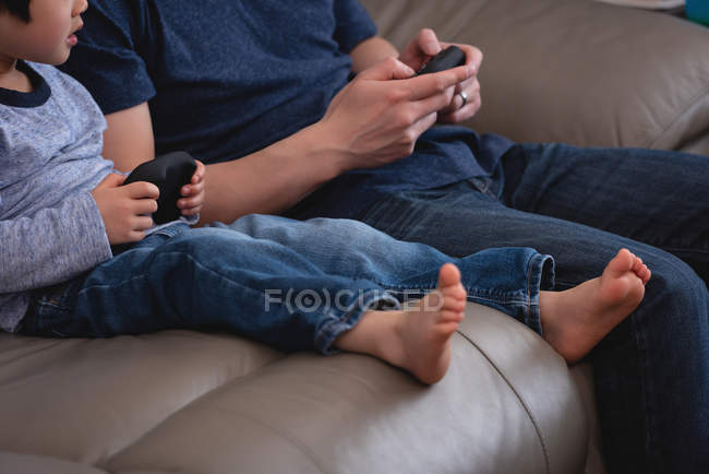 Mid section of Asian father and son playing video games together while sitting on sofa at home — Stock Photo