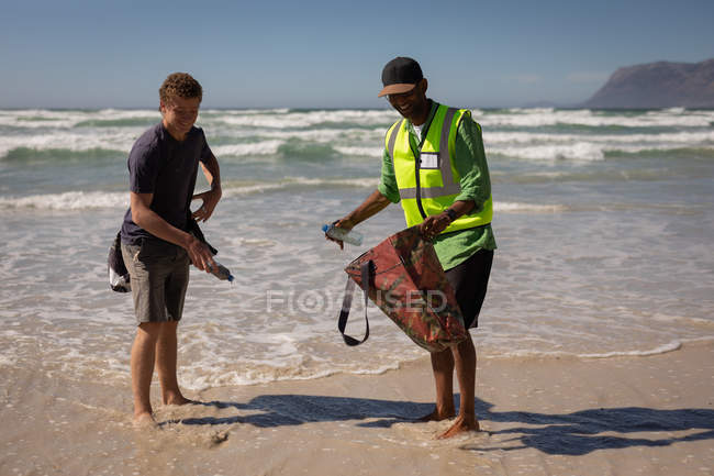 Vista frontale dei volontari afroamericani maschi che puliscono la spiaggia in una giornata di sole — Foto stock