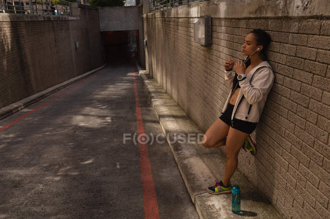 Seitenansicht einer jungen Frau mit gemischter Rasse, die auf der Straße über Kopfhörer Musik hört — Stockfoto