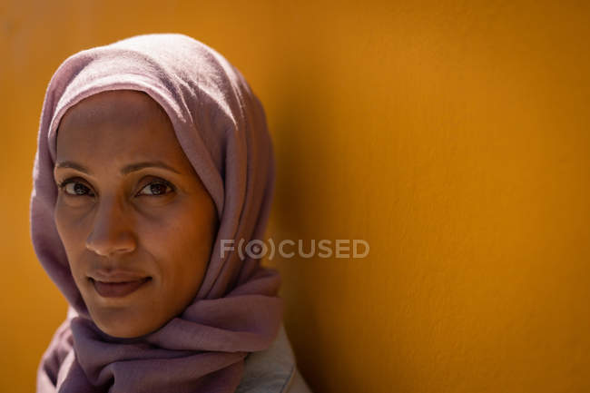 Porträt einer schönen Mischlingsfrau mit Hijab, die an einem sonnigen Tag an die Wand lehnt — Stockfoto