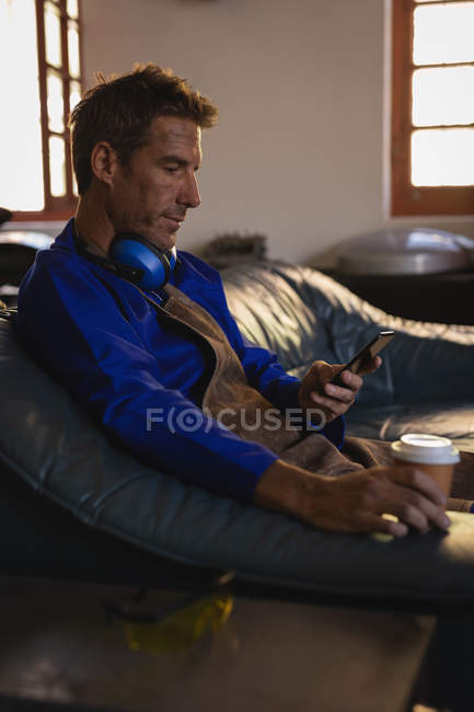 Side view of Caucasian male bike mechanic using mobile phone while having coffee in garage — Stock Photo