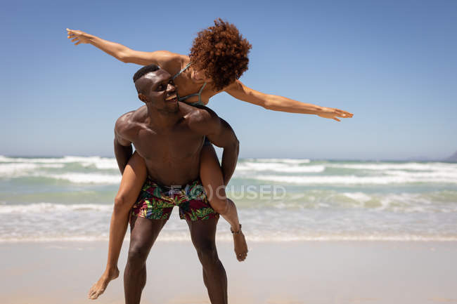 Вид спереди счастливого афроамериканца и женщины смешанной расы, стоящих в позе свиньи на пляже в солнечный день — стоковое фото