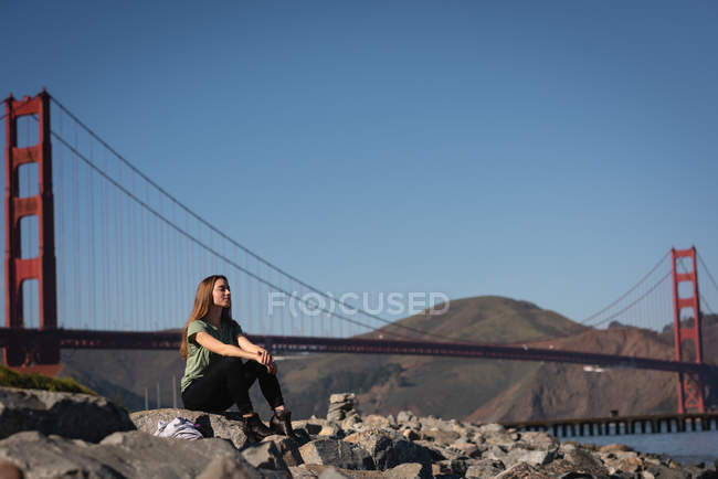 Вид спереду красива жінка, що сидить на скелі біля мосту золотих воріт — стокове фото