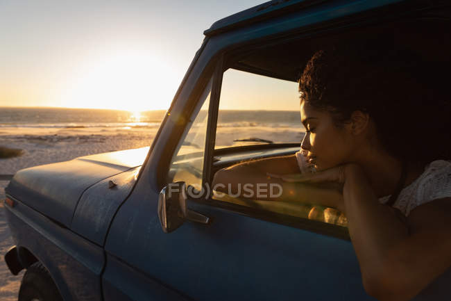 Вид збоку красивою молодої афроамериканської жінки мріють, сидячи в машині на пляжі на заході сонця — стокове фото