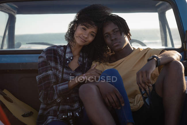 Vista frontal do jovem casal romântico afro-americano sentado em carro na praia em um dia ensolarado — Fotografia de Stock