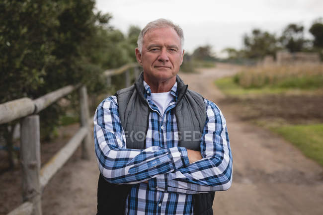 Portrait of senior Caucasian male farmer standing arms crossed on farm road — Stock Photo