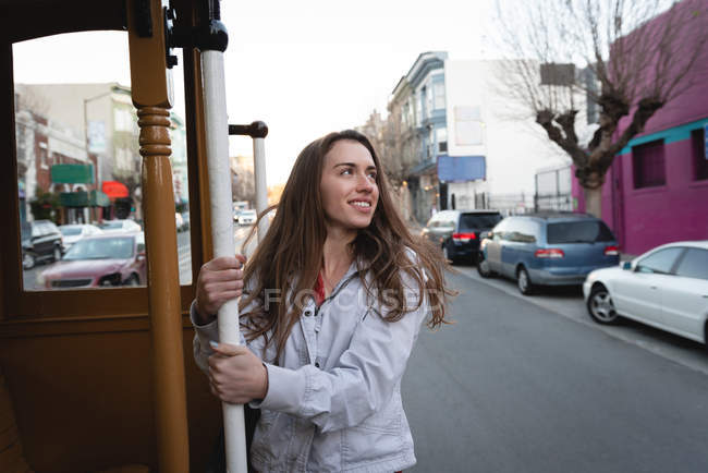 Vue de face de heureuse jeune femme caucasienne suspendue à l'extérieur du véhicule en mouvement en ville — Photo de stock