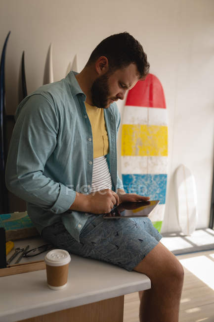 Seitenansicht eines aufmerksamen kaukasischen Mannes mit Laptop, während er Kaffee trinkt und in einer Werkstatt auf dem Tisch sitzt — Stockfoto