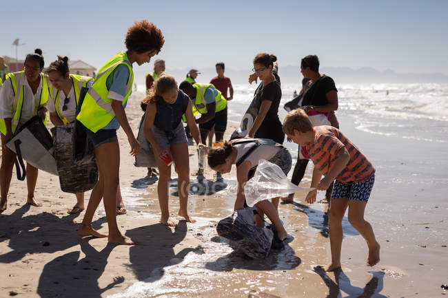 Вид спереду групи багатонаціональних добровольців, що прибирають пляж у сонячний день — стокове фото