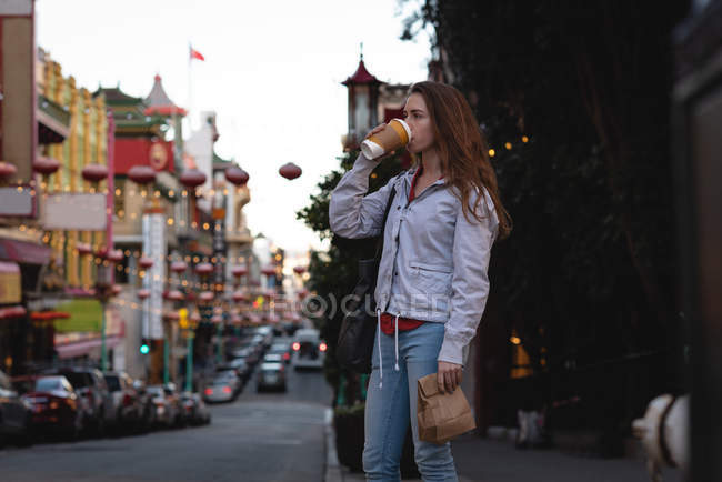 Вид збоку красива молода кавказька жінка з кавою, стоячи на вулиці в місті — стокове фото