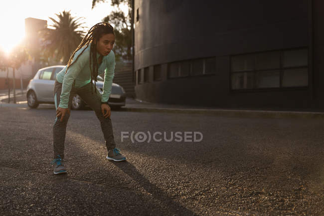 Vue de face de la jeune femme fatiguée de race mixte se reposant après l'exercice dans la ville — Photo de stock