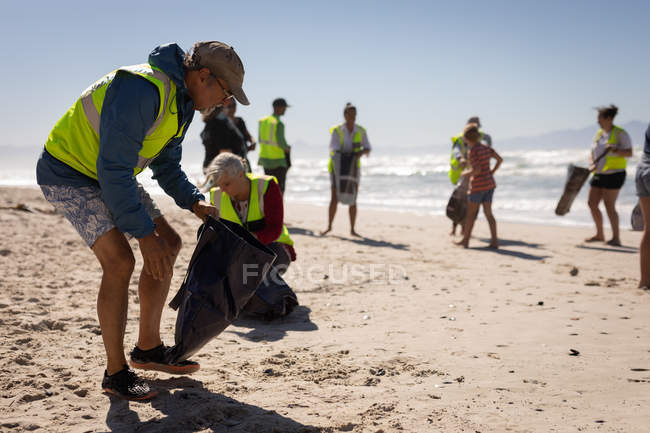 Вид на группу мультиэтнических волонтеров, убирающих пляж в солнечный день — стоковое фото