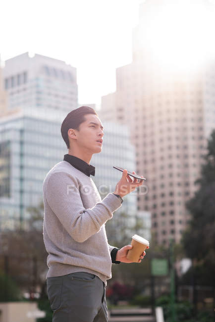 Вид сбоку хорошо выглядящего азиатского мужчины, разговаривающего по мобильному телефону, стоя на улице — стоковое фото