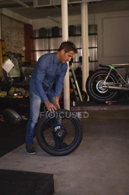 Vue latérale du mécanicien de vélo masculin caucasien tenant le pneu tout en se tenant dans le garage — Photo de stock