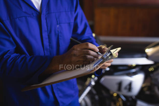 Sección media del mecánico de bicicletas manteniendo registros de automóviles en el portapapeles en el garaje - foto de stock