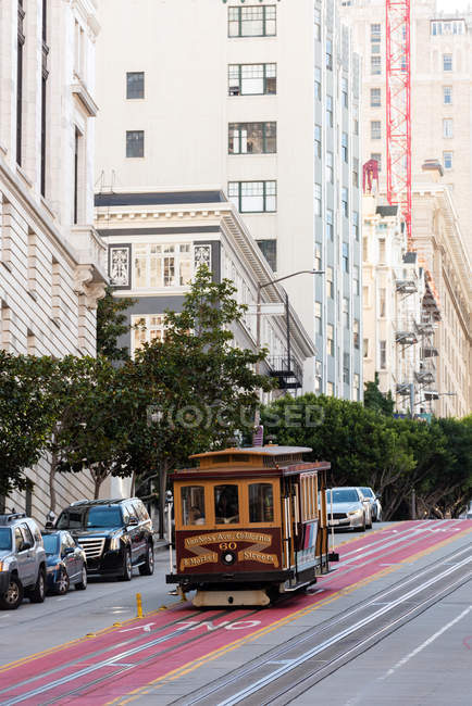 Трамвай движется по тропе через городскую улицу в солнечный день — стоковое фото