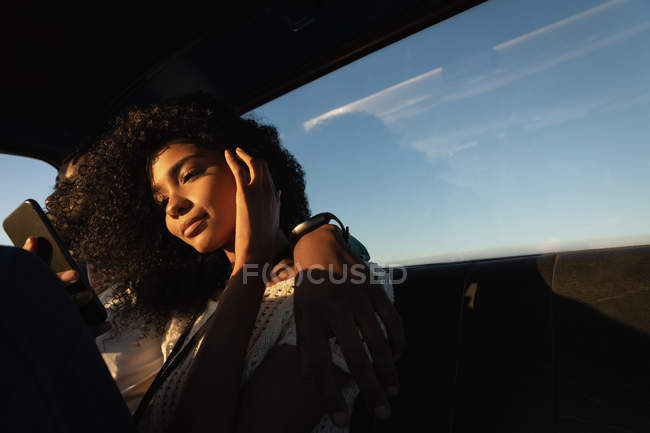 Niedrigwinkel-Ansicht der schönen jungen afrikanisch-amerikanischen Frau mit Handy, während sie neben ihrem Freund im Auto sitzt — Stockfoto