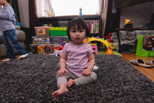 Porträt eines kleinen süßen asiatischen Babys, das in die Kamera schaut und zu Hause auf Teppich sitzt — Stockfoto