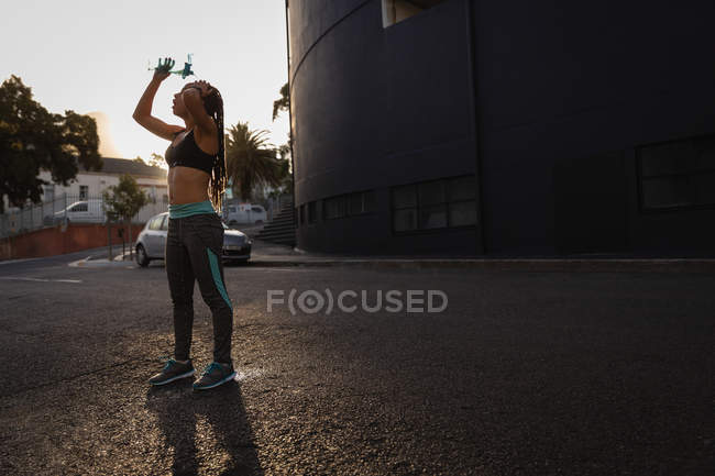 Vue latérale de jeune femme de race mixte en forme versant de l'eau sur sa tête dans la rue — Photo de stock