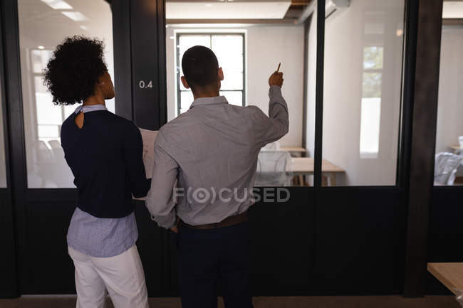 Вид ззаду молодих бізнесменів змішаної раси, які обговорюють синій друк в офісі, в той час як один з них показує щось перед ним — стокове фото