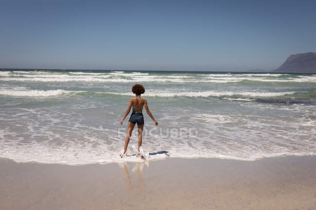 Вид на молодую женщину смешанной расы, стоящую на пляже в солнечный день — стоковое фото