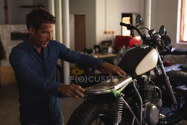 Vista lateral de hombre caucásico mecánico de bicicleta fijación de asiento nuevo en moto en el garaje - foto de stock
