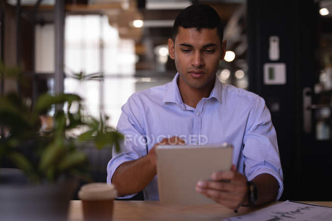 Вид спереду красивий молодий бізнесмен змішаної раси, використовуючи цифровий планшет за столом в сучасному офісі — стокове фото