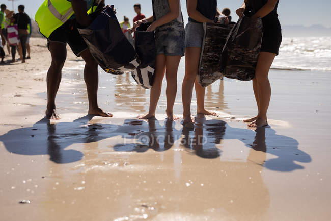 Baixa seção de grupo de voluntários limpeza praia em um dia ensolarado — Fotografia de Stock