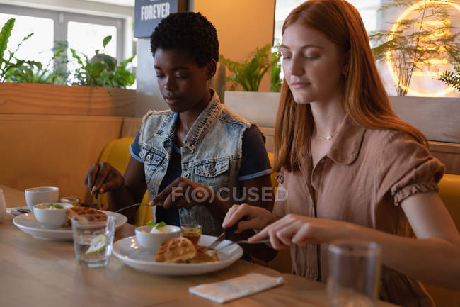 Vista lateral de amigos femeninos de raza mixta sentados en el restaurante mientras desayunan - foto de stock