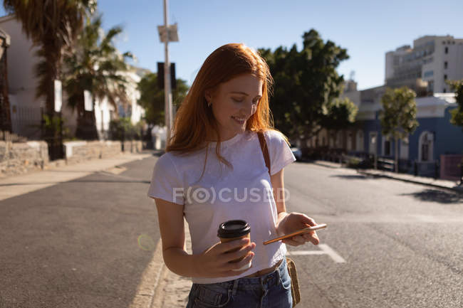 Вид спереди на красивую молодую кавказскую женщину, пользующуюся мобильным телефоном за чашечкой кофе на улице в солнечный день — стоковое фото