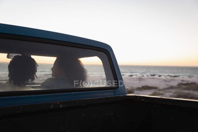 Rear view of romantic couple sitting in a car on the beach at sunset — Stock Photo