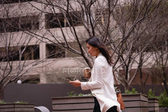 Side view of Asian woman using mobile phone while walking on the sidewalk — Stock Photo