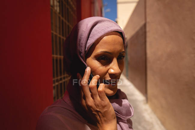 Vue de face de belle femme mixte parlant sur téléphone portable tout en se tenant dans l'allée par une journée ensoleillée — Photo de stock