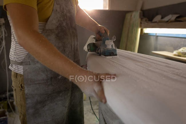 Mid section of man shaping surfboard in a workshop. — Stock Photo