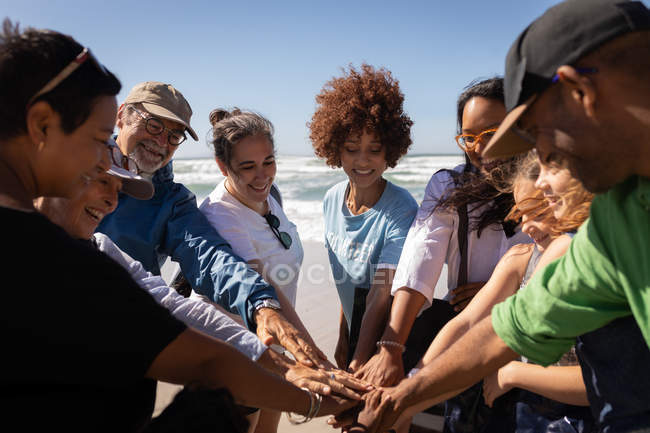 Vue de face de plusieurs groupes ethniques de bénévoles formant une pile de main sur la plage — Photo de stock