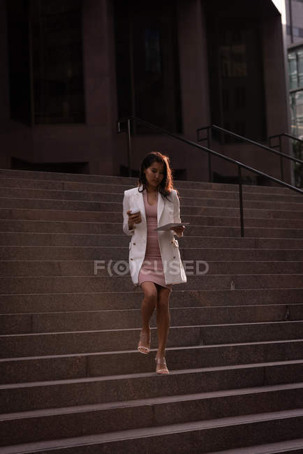 Niedrigwinkel-Ansicht einer jungen asiatischen Frau, die ein digitales Tablet benutzt, während sie Treppen hinuntergeht — Stockfoto