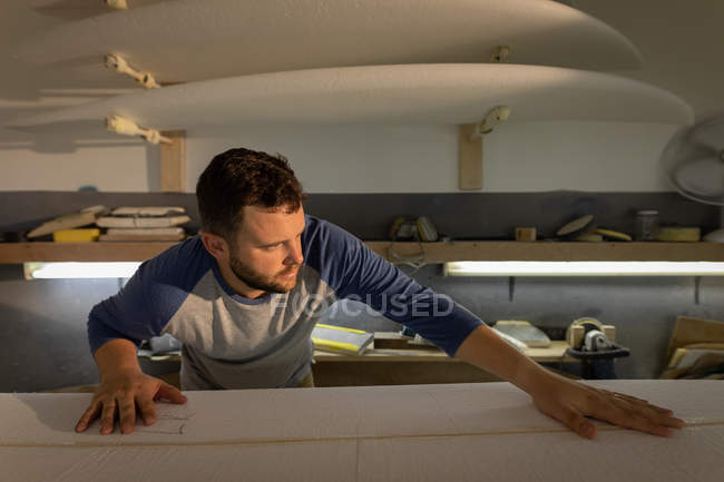 Front view of Caucasian man checking and if the surfboard is smooth and ready for painting in a workshop — Stock Photo
