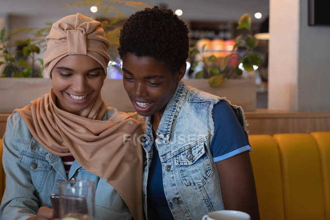 Вид з красивих афро-американських жінок друзів за допомогою мобільного телефону, сидячи в ресторані — стокове фото