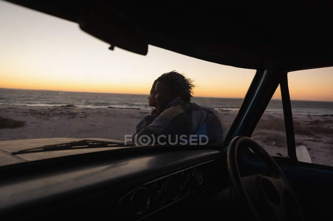Vue latérale d'un couple romantique debout près d'une voiture sur la plage au coucher du soleil — Photo de stock