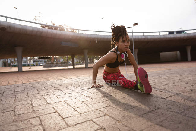 Vue de face de la forme jeune femme mixte faisant de l'exercice d'étirement dans la rue — Photo de stock